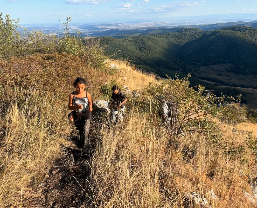 Two girls hiking up a grassy mountain ridge in the evening sun