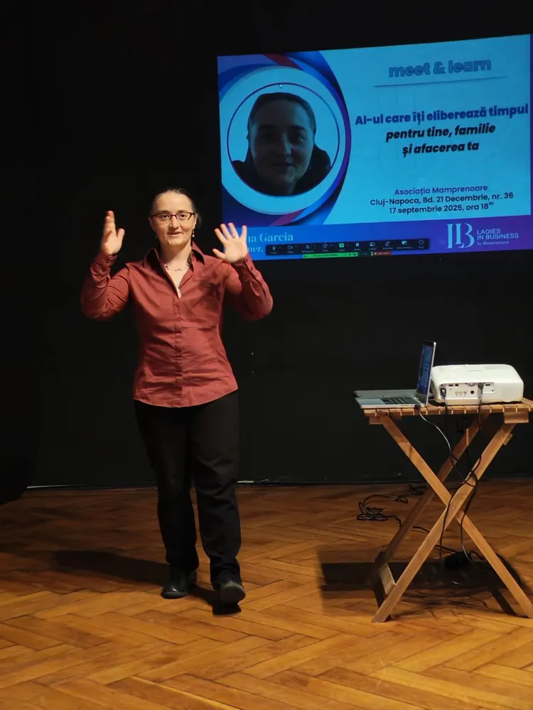Oana Garcia on a wooden stage with her arms raised, giving a talk about AI at a meet & learn event in Cluj