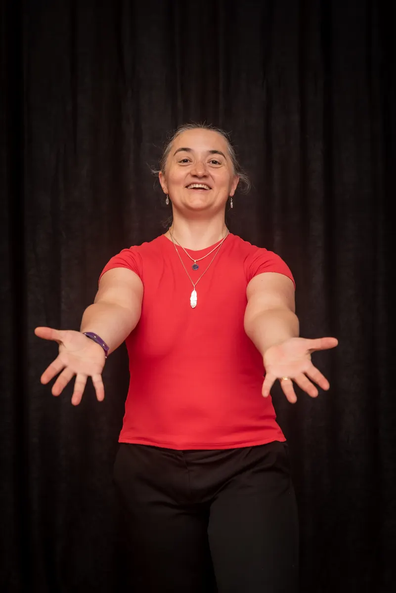 Oana Garcia in a red top, smiling with her arms open in welcome